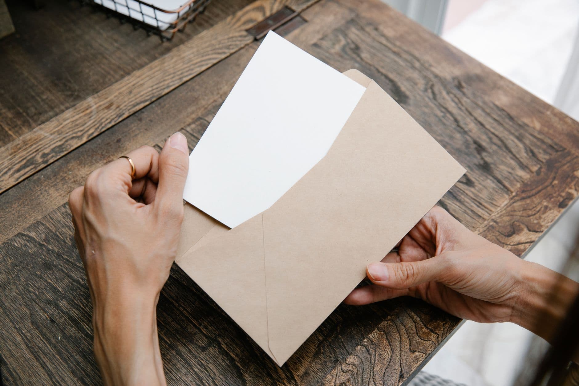 Handen halen een brief uit een bruine envelop op een houten tafel