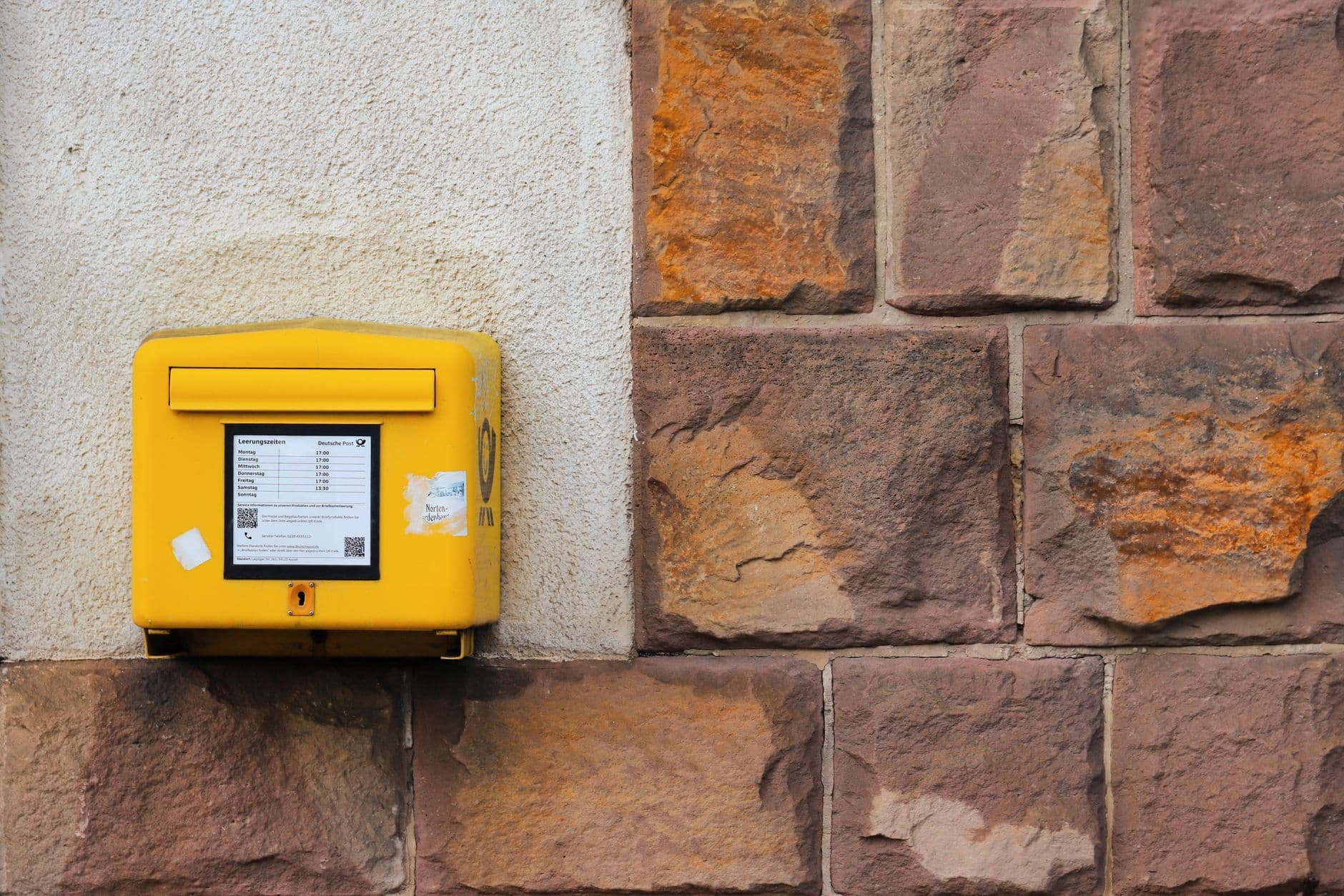 Gelber Briefkasten der Deutschen Post an einer Hauswand aus Sandstein